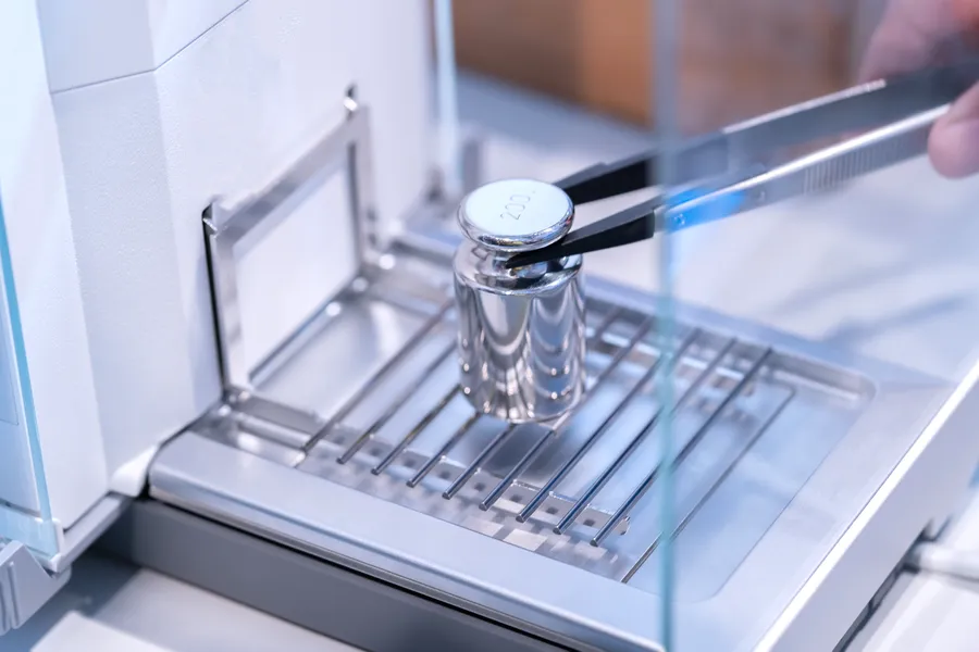 Calibration weight being placed on an analytical balance with tweezers